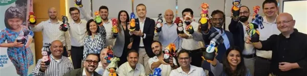 A diverse group of people holding colorful crafts, celebrating together in a bright office space. A banner visible in the background.