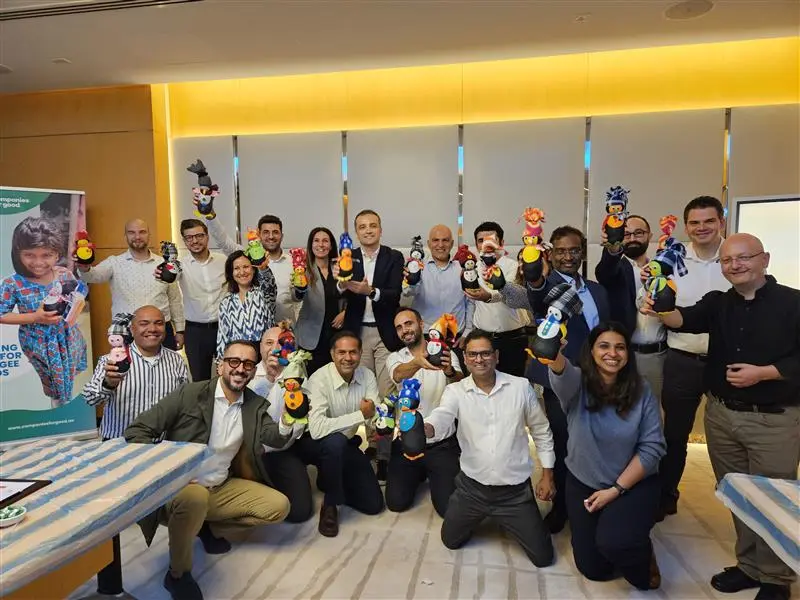 A diverse group of people holding colorful crafts, celebrating together in a bright office space. A banner visible in the background.