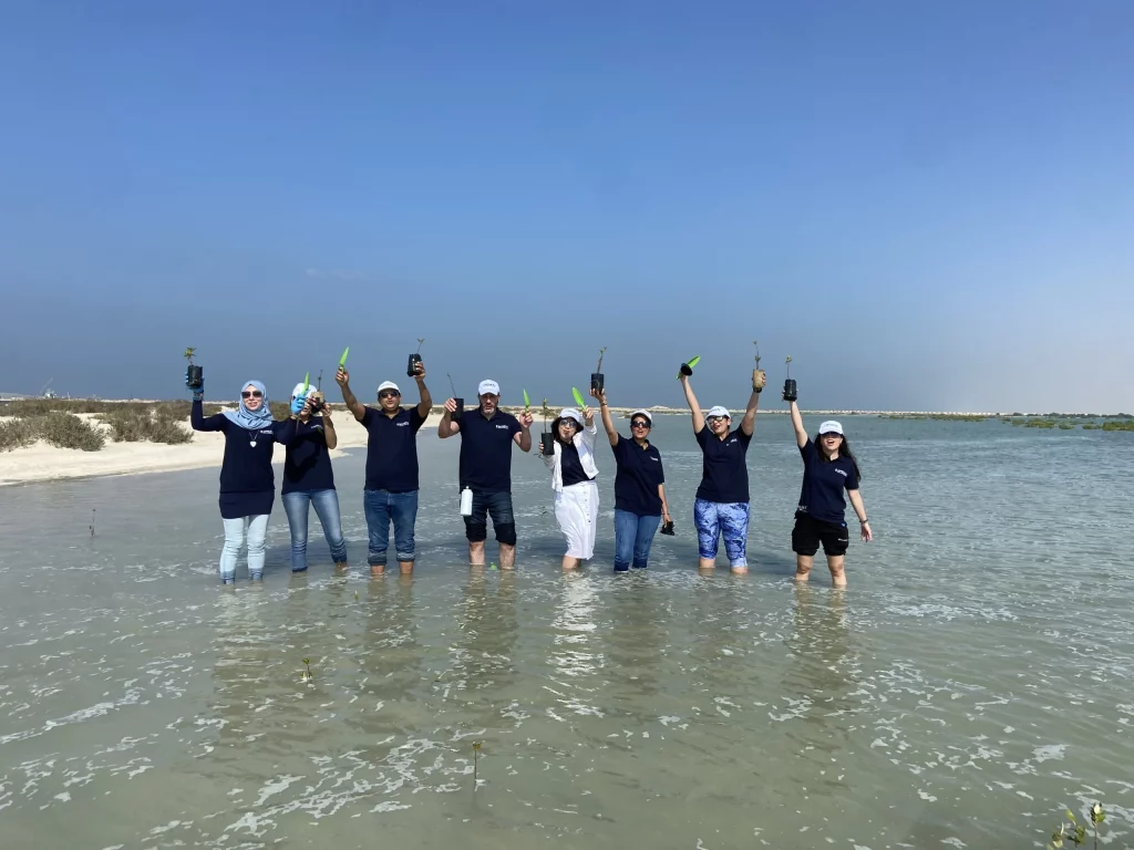 A group of individuals standing in water, raising their hands to show ghaf planting