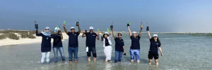 A group of individuals standing in water, raising their hands to show ghaf planting