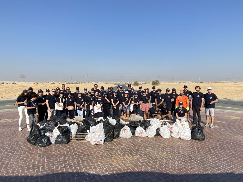 Group of individuals stands with collection of garbages after desert cleaning