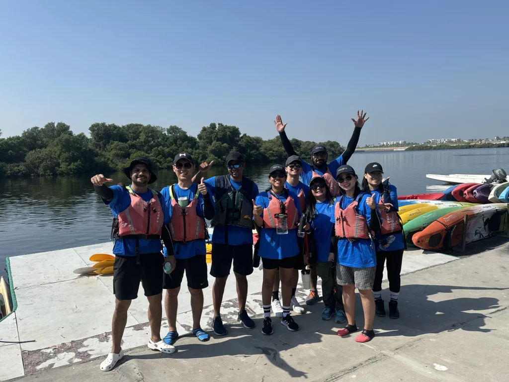 A group of happy kayakers in life jackets ready to paddle, near colorful kayaks by a lake.