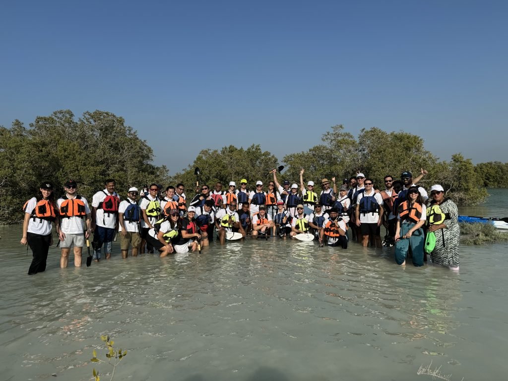 A large group of people with life jackets standing in water, outdoors, raising hands in celebration.