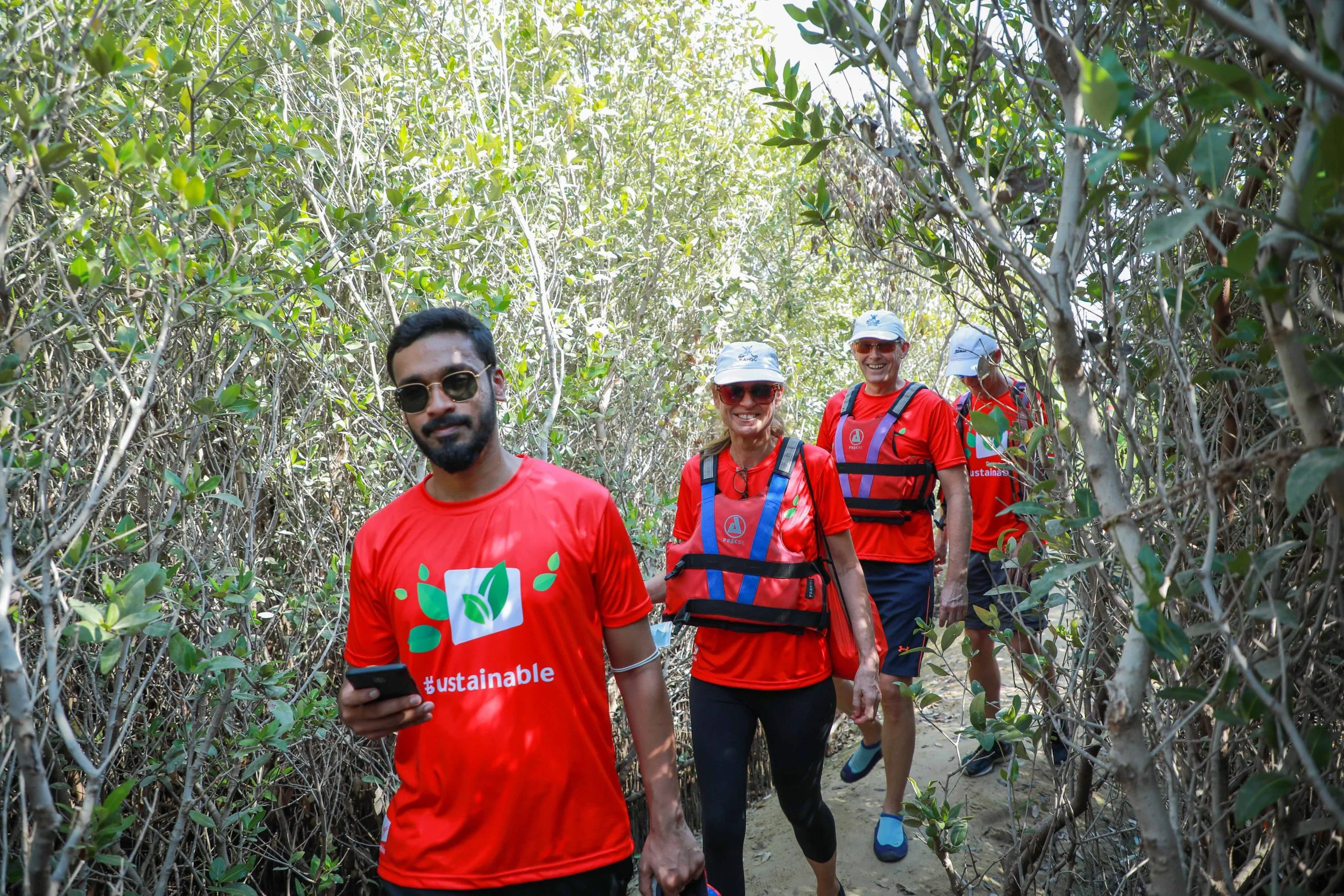 Group of individuals wearing red shirts walking through a mangrove forest.