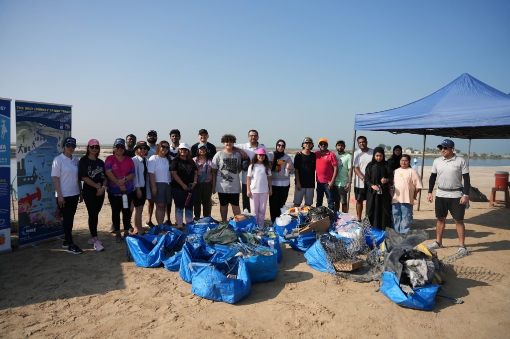 Group of volunteers by the water after a clean-up event, with collected trash bags and a blue tent.