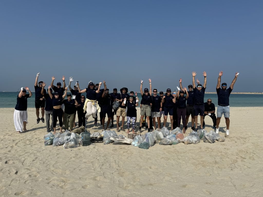 Group of people celebrating a beach cleanup, raising tools and trash bags in the air.