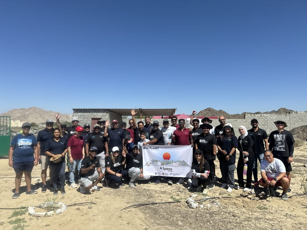 A group of people posing outdoors with a banner, under a clear sky with hills in the background.