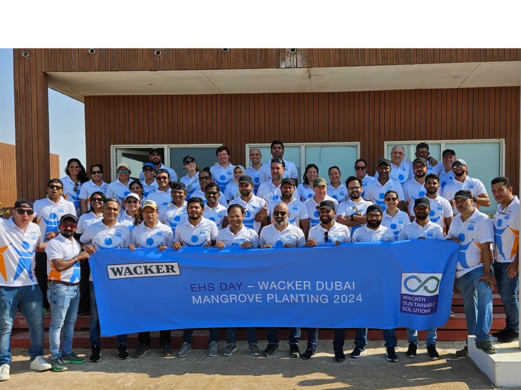 A group of people in matching shirts posing with a "WACKER" banner in front of a building.