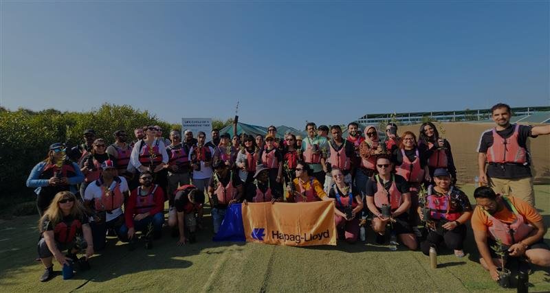 A large group of people wearing life jackets gathers outdoors, smiling and posing for a photo under clear blue skies.