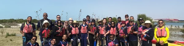 A group of environmental volunteers in life jackets poses with saplings near a waterway, ready for a tree-planting initiative.