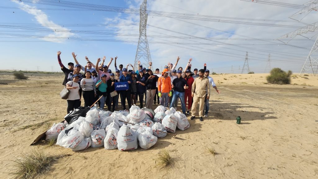 A group of volunteers celebrates after a clean-up event, standing in front of collected trash bags in a desert landscape.