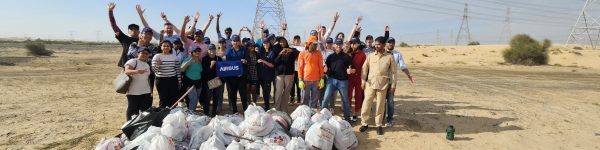 A group of volunteers celebrates after a clean-up event, standing in front of collected trash bags in a desert landscape.