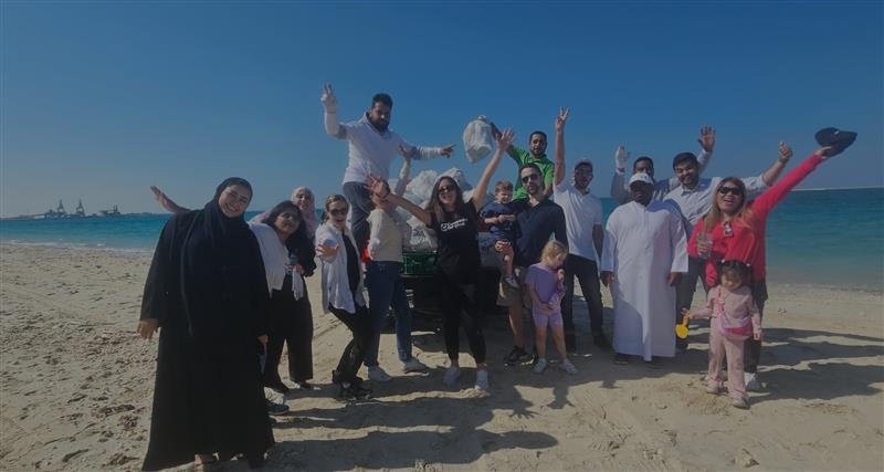 A diverse group of people joyfully celebrating on a sunny beach, with the sea and a clear blue sky in the background.