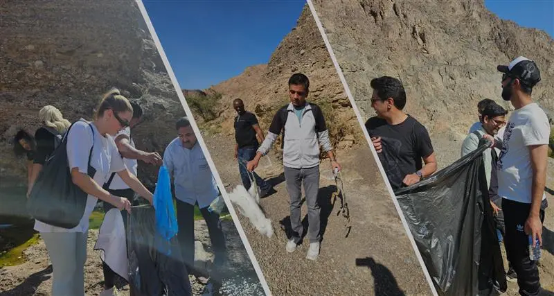 A group of individuals participates in an outdoor clean-up, collecting waste and engaging with the environment in a sunny location.