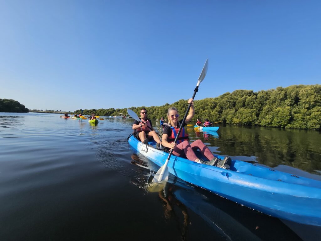 A group of kayakers paddles through calm waters surrounded by lush greenery under a clear blue sky.