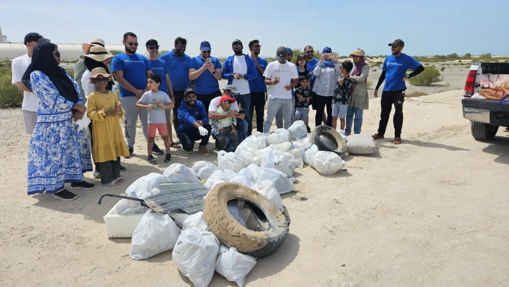 A diverse group of volunteers poses proudly beside bags of collected trash and used tires, showcasing their beach cleanup efforts.