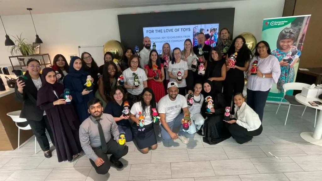 A diverse group of people proudly holding handmade dolls, gathered in a modern indoor space for a fun community event.