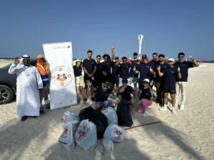 A diverse group of volunteers stands on a beach beside a truck filled with collected trash, promoting environmental clean-up efforts.
