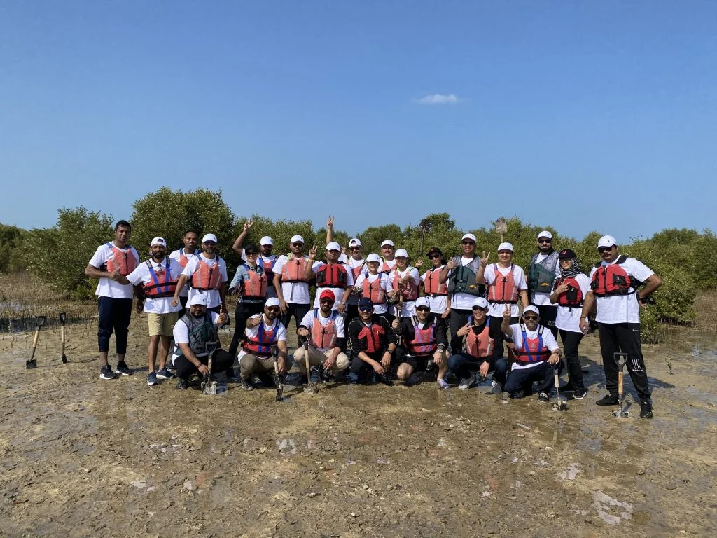 Group of people wearing life vests posing outdoors on muddy ground during a mangrove planting activity