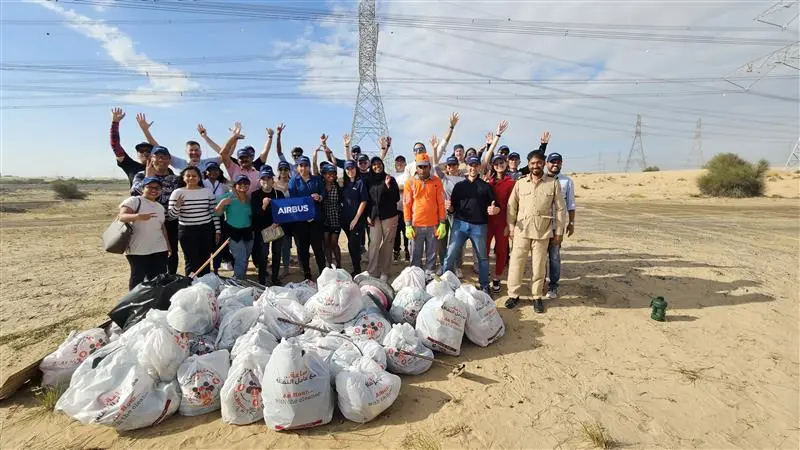 A diverse group of volunteers smiles and poses with raised arms, celebrating their successful cleanup effort in a desert area.