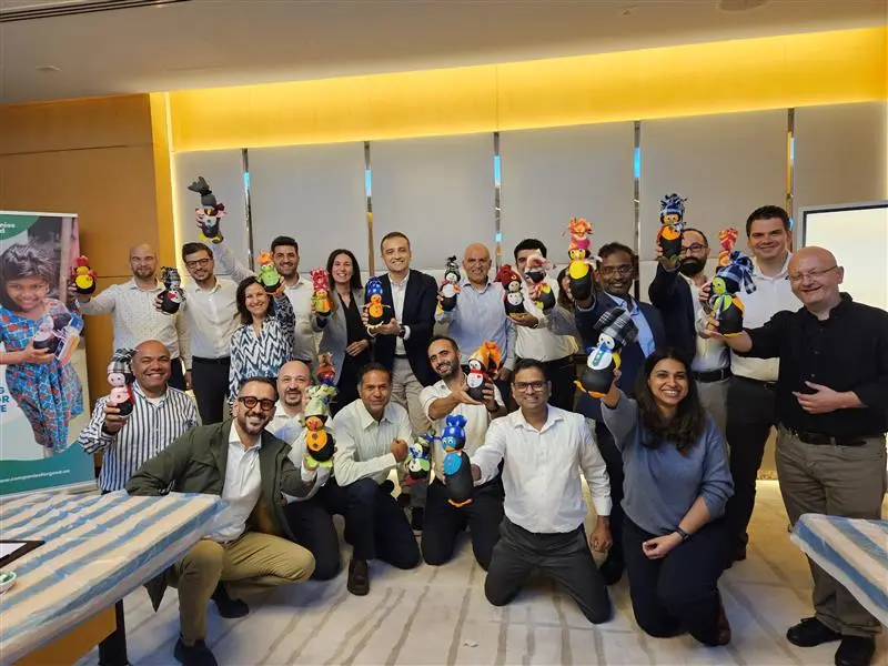 Group of professionals smiling and proudly holding up colorful handcrafted dolls during a corporate volunteering or team activity