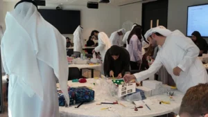 A diverse group of people in traditional dress collaborates around tables filled with materials in a creative workshop setting.