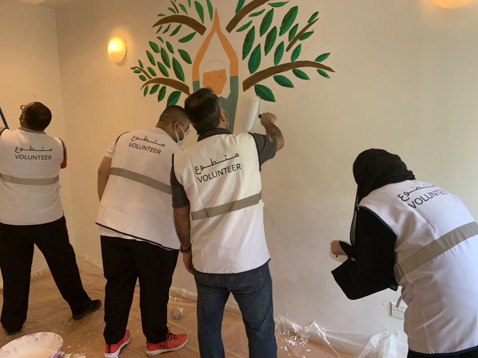 Volunteers painting tree mural on wall