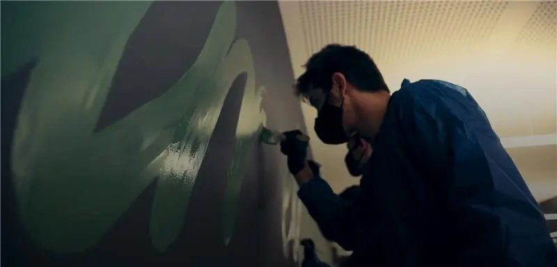Masked painter adding green mural to wall